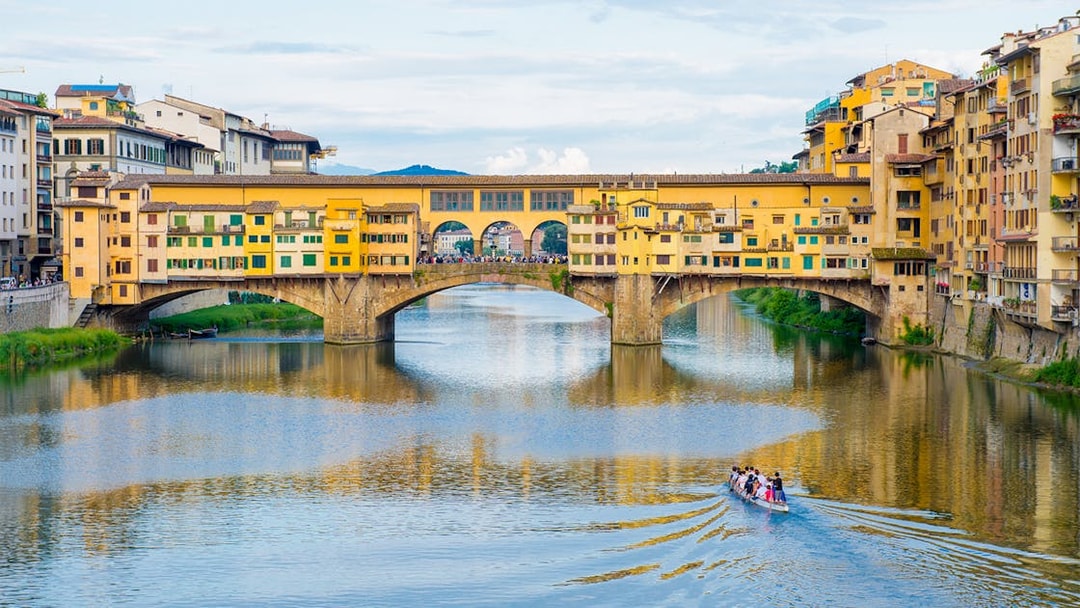 Ponte Vecchio bridge over Arno River in Florence with a boat tour passing underneath.