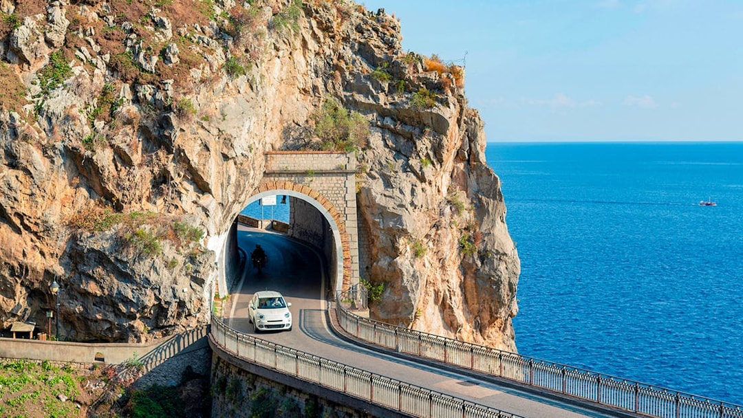 Car driving through a coastal tunnel on the Amalfi Coast with sea views.