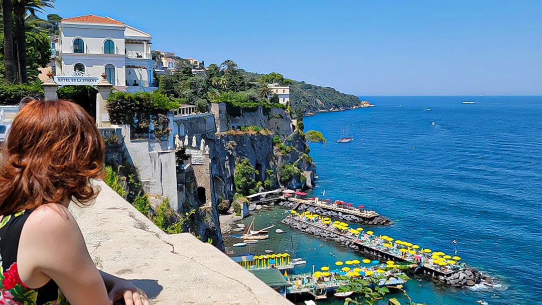 Woman overlooking Amalfi Coast with colorful beach umbrellas and cliffs.