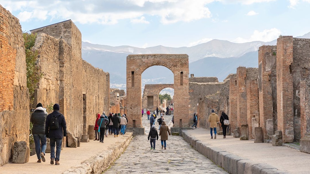 Tourists walking through ancient Pompeii ruins with audio guides.