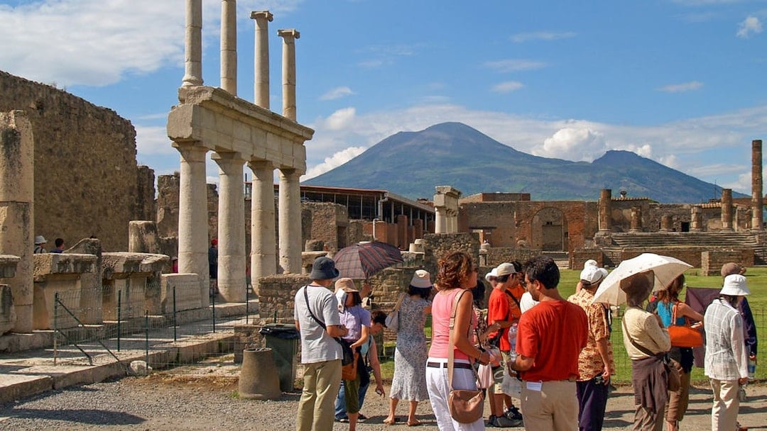 Tourists exploring ancient ruins in Pompeii with Mount Vesuvius in the background.