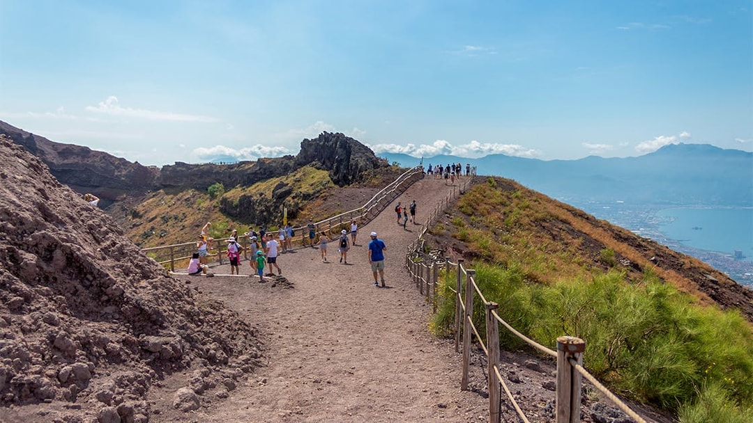 Hikers walking along a trail on Mount Vesuvius with views of the surrounding landscape.