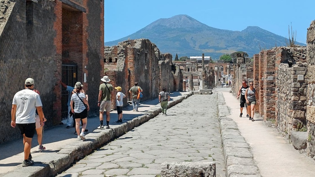 Visitors exploring ancient streets of Pompeii with Mount Vesuvius in the background.