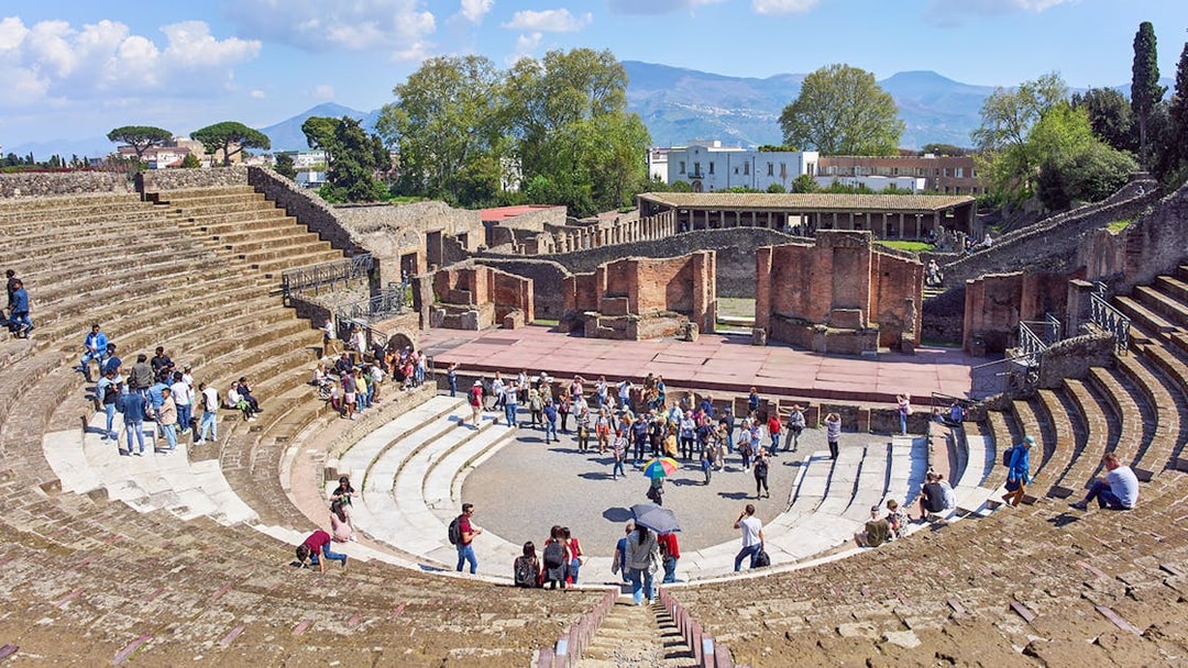 Tourists exploring the ancient amphitheater ruins in Pompeii under a clear blue sky.