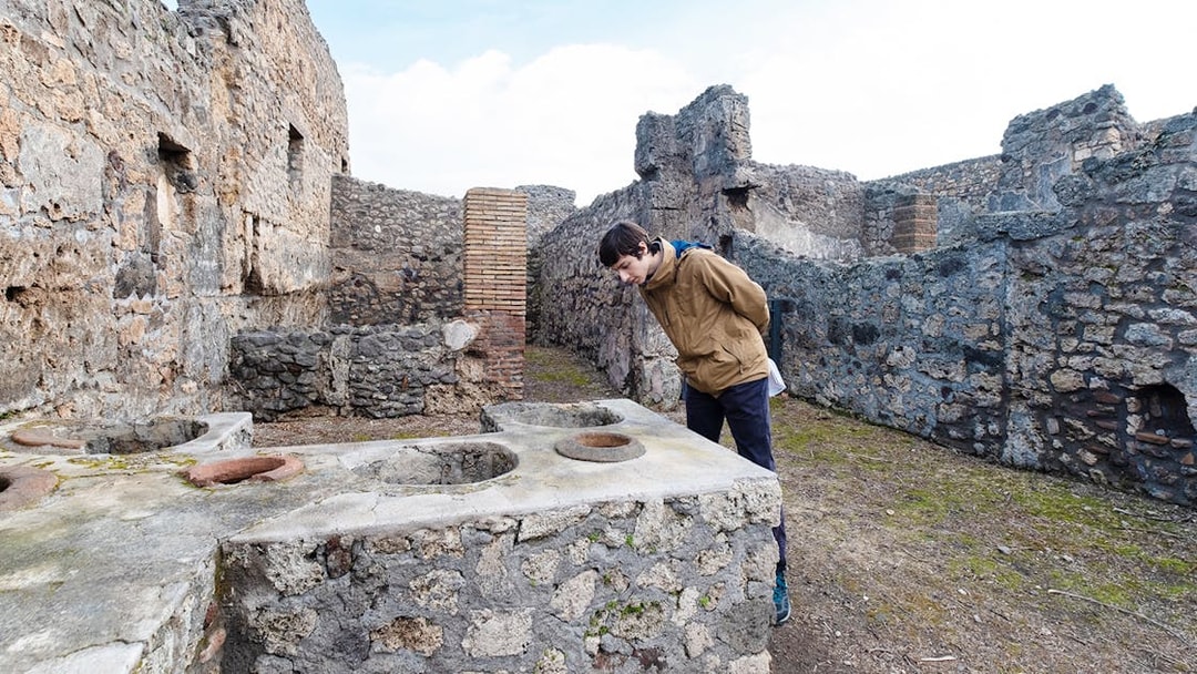 Visitor examining ancient counter at Termopolium in Pompeii ruins.