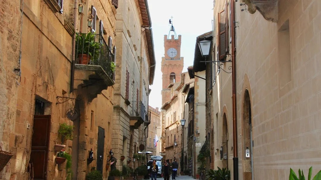 Narrow street in Tuscany with historic buildings and a clock tower in the distance.