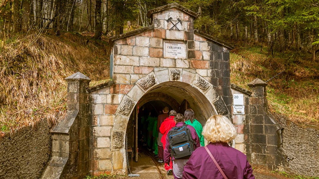 Visitors entering Salzwelten salt mines through stone archway in forest setting.