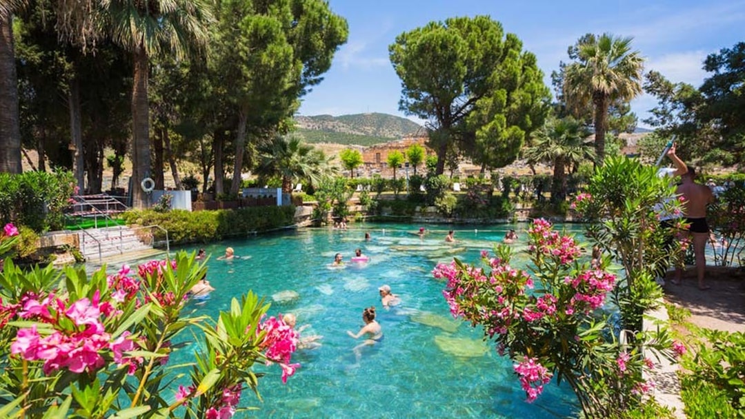 People swimming in the thermal pool surrounded by trees and flowers in Pamukkale, Turkey.