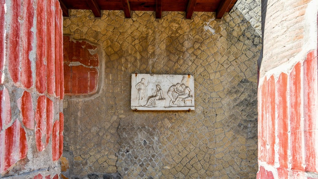 Ancient fresco in Herculaneum with red columns and stone wall, seen on a Sorrento tour.