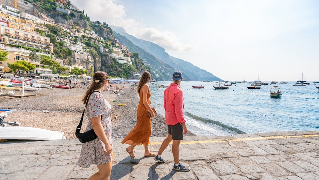 People walking along the Amalfi Coast with boats on the sea.