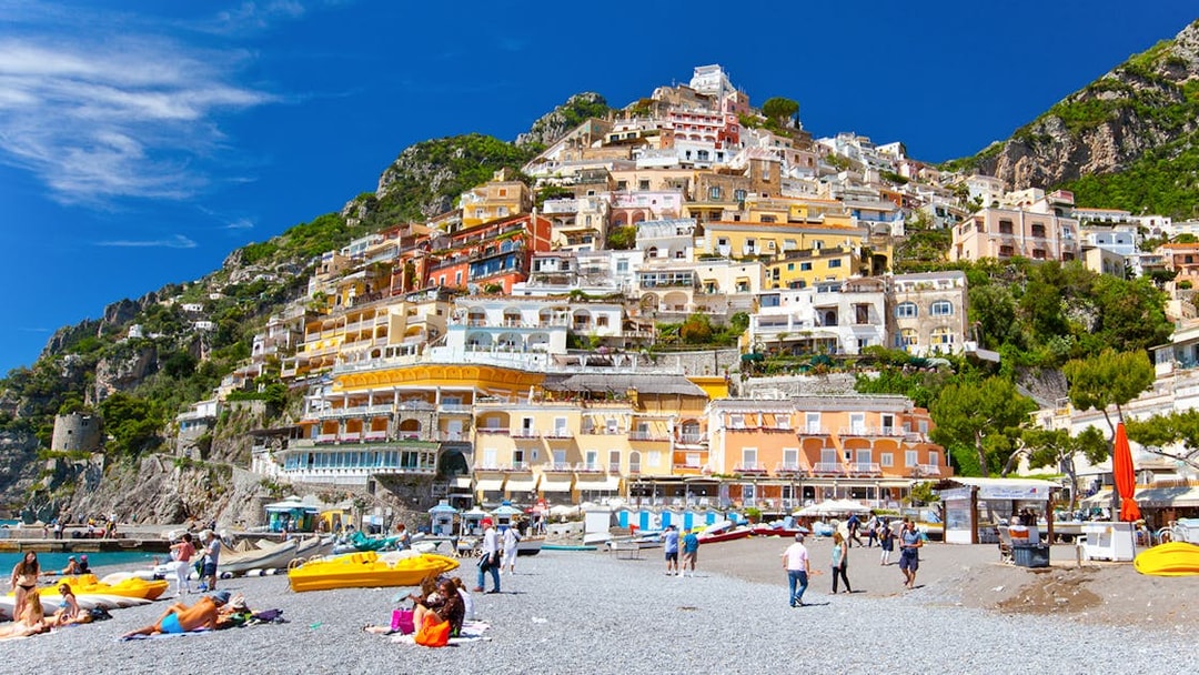 Colorful hillside buildings overlooking Positano beach with people relaxing on the shore.