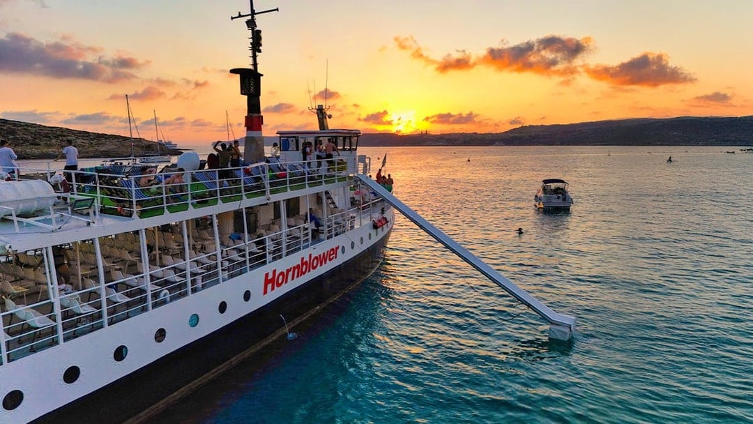 Cruise ship at sunset in Blue Lagoon, Malta with passengers on deck.