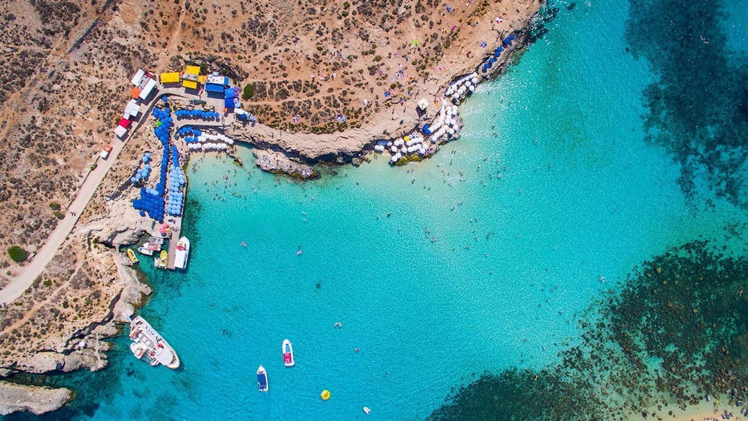 Aerial view of Blue Lagoon, Malta with boats and sunbathers along the rocky coastline.