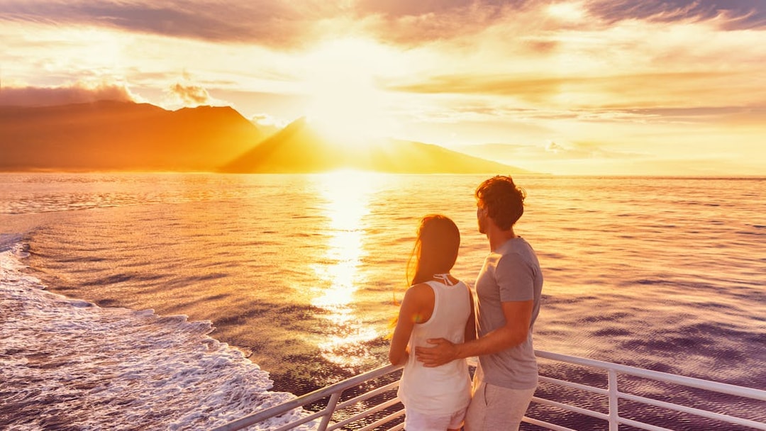 Couple enjoying sunset on a sailing cruise with ocean and mountains in view.