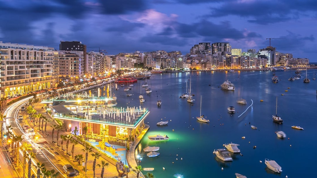 Night view of Sliema Bay, Malta with illuminated waterfront and boats.