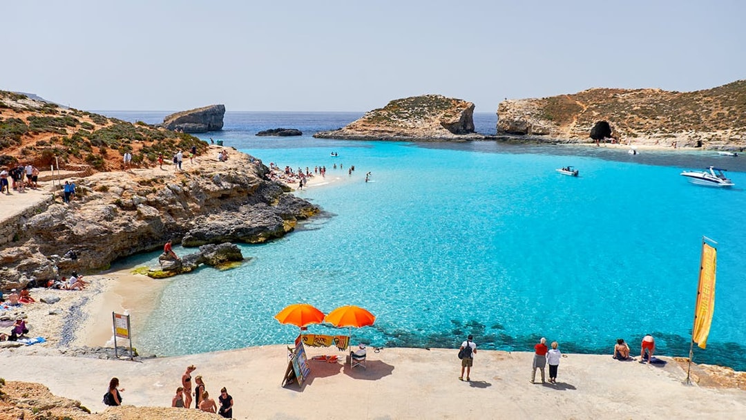 Visitors enjoying the clear waters of Blue Lagoon, Malta with boats and rocky cliffs in the background.