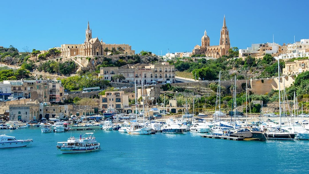 Harbor view of Gozo with boats and historic buildings on a hillside.