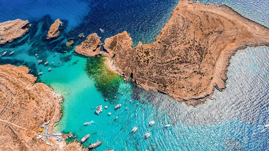 Aerial view of boats in the Blue Lagoon, Malta, surrounded by clear turquoise water and rocky coastline.