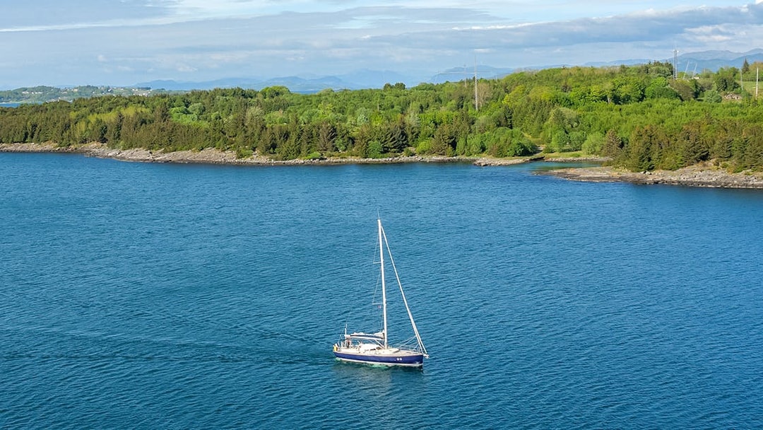 Sailboat on Stavanger Fjord with lush green shoreline in the background.
