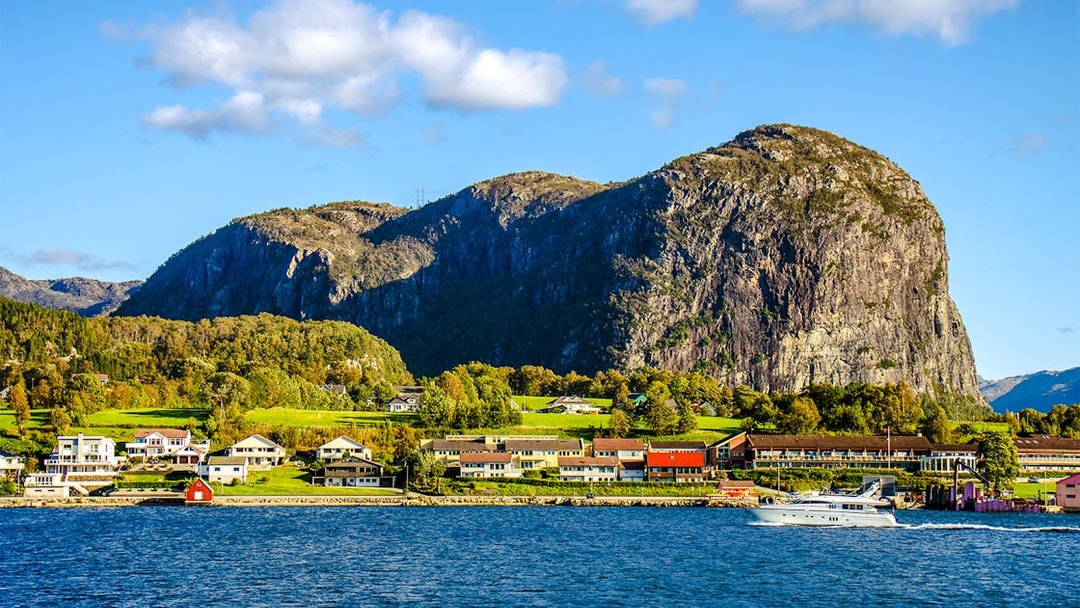 Houses along the shore with a boat on Lysefjord, Norway, and rocky cliffs in the background.