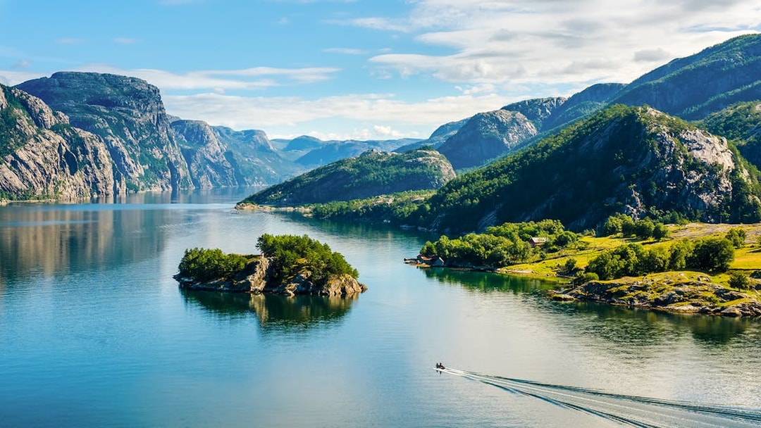 Lysefjord in Norway with lush green mountains and a small boat on the water.