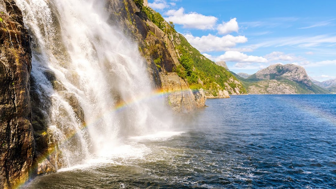 Waterfall cascading into Lysefjord with a rainbow, Lysefjord, Norway.