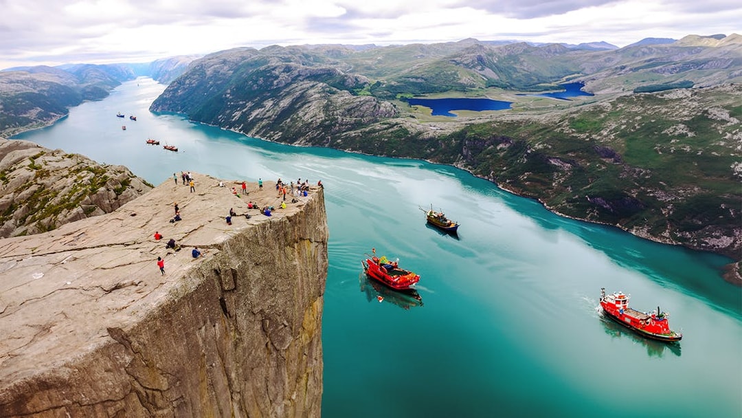 Visitors on Preikestolen Cliff overlooking Lysefjord, Norway, with boats in the water below.