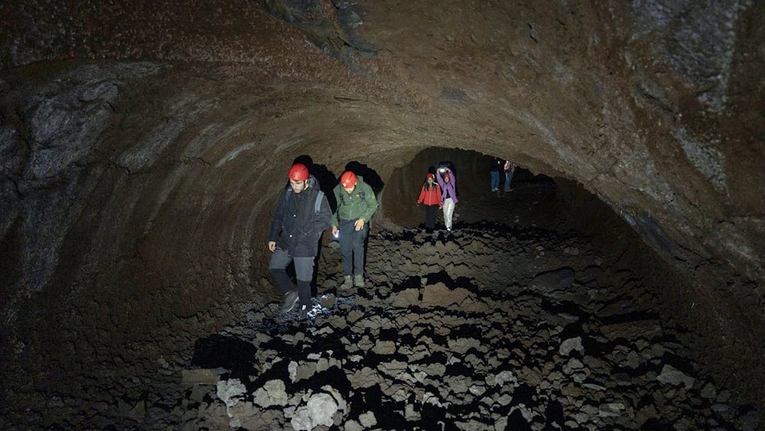 Visitors exploring Mount Etna lava cave with helmets and flashlights.