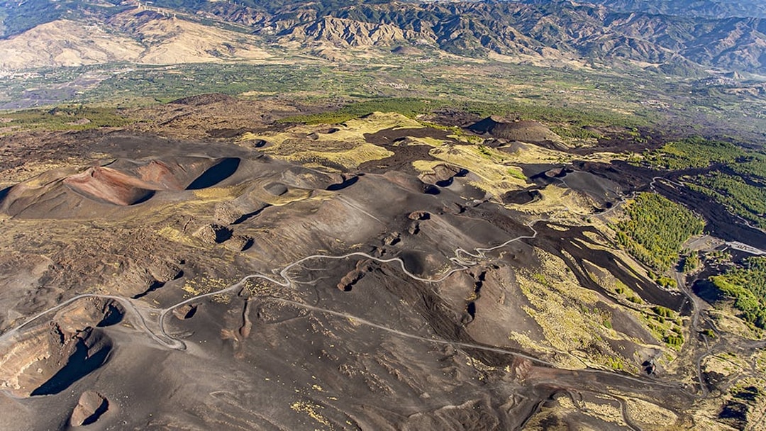 Aerial view of Mount Etna's volcanic landscape with winding roads and craters, Sicily, Italy.
