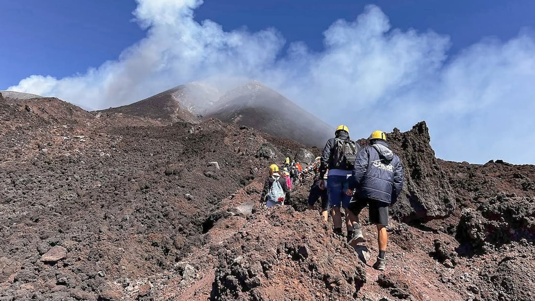 Hikers ascending rocky path towards Mount Etna summit, Sicily.