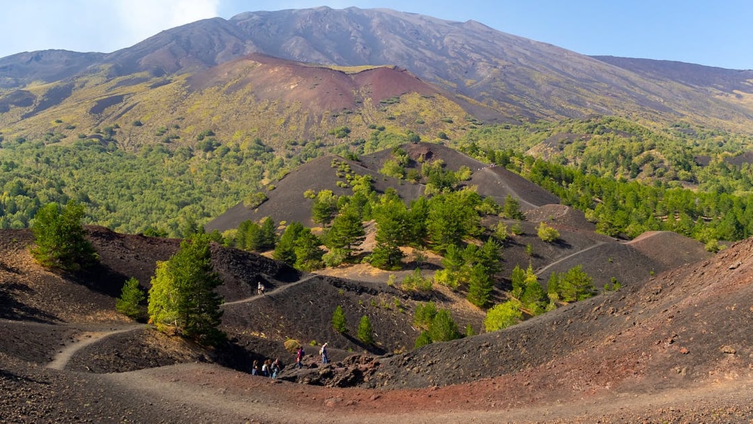 Mount Etna north slopes with side crater and hikers on volcanic terrain.