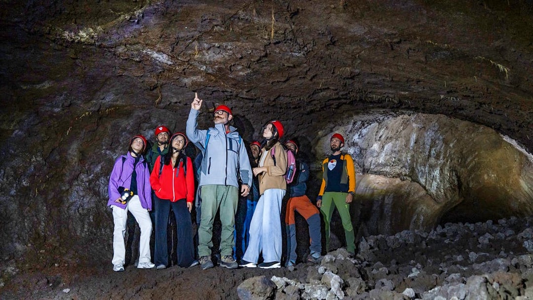 Group exploring a lava cave on Mount Etna during a morning tour in Catania.