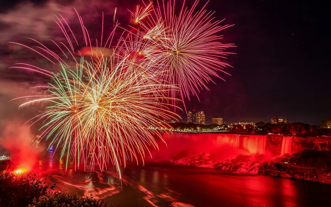 Fireworks display over illuminated Niagara Falls at night.