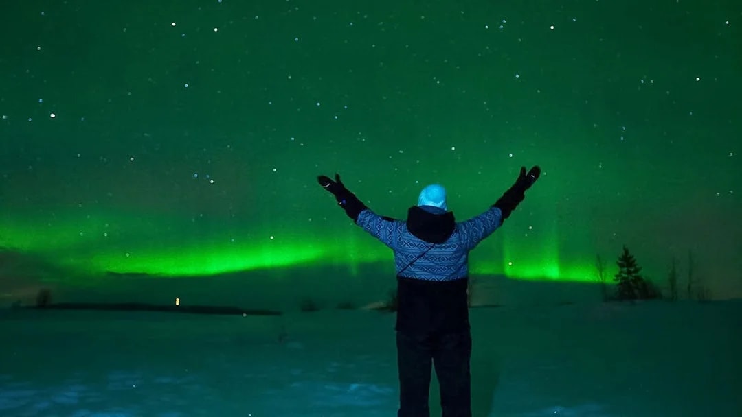 Person admiring Northern Lights over snowy Tromso landscape.