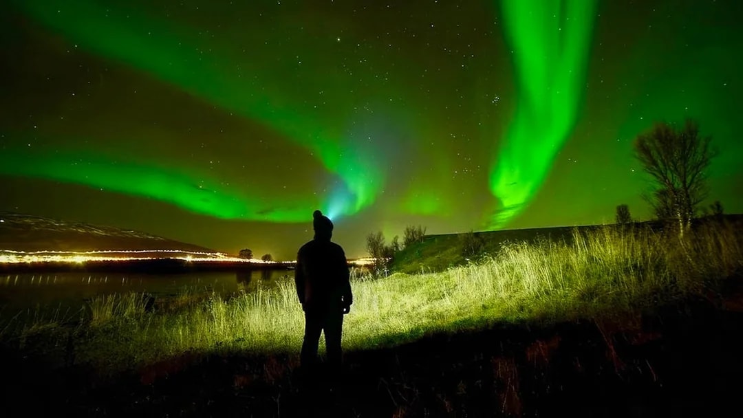 Person watching Northern Lights in night sky during aurora borealis tour.