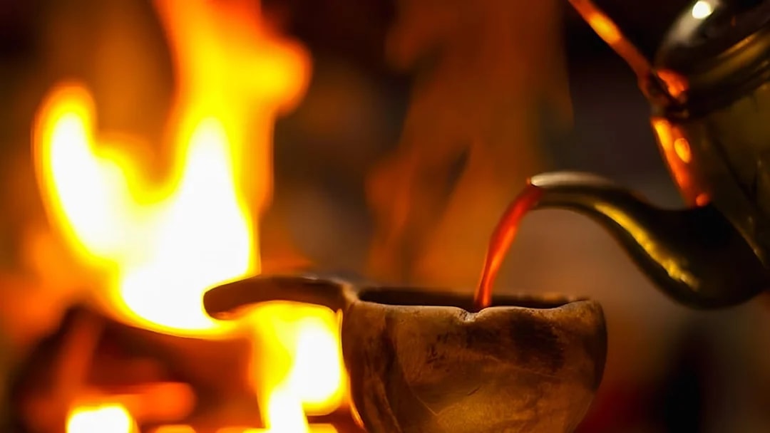 Warm drink being poured into a wooden cup by a fire during Northern Lights tour.
