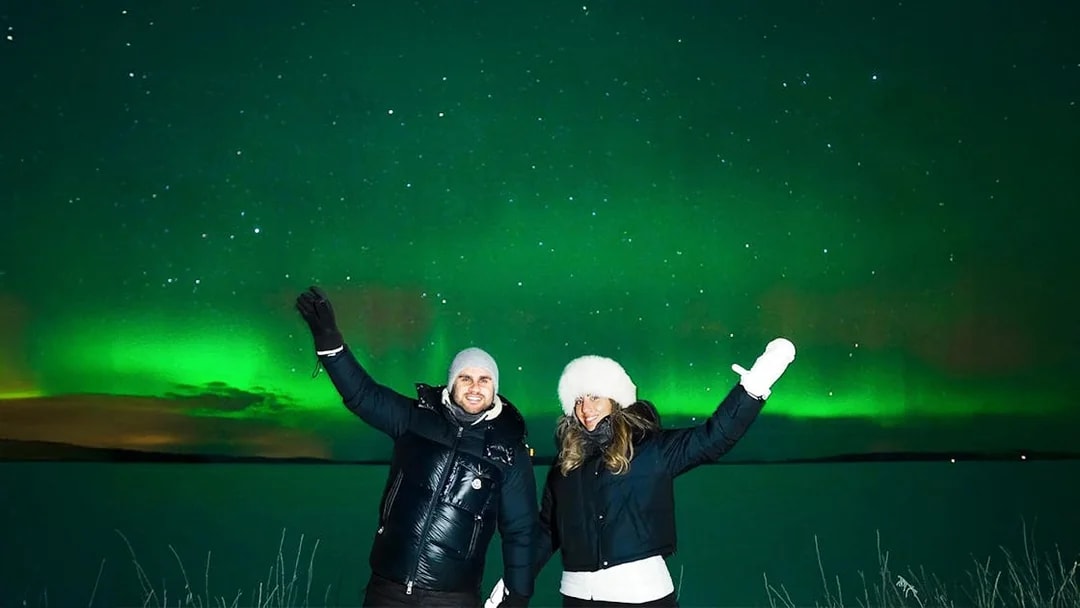 Northern Lights over snowy landscape with two people on Tromso Northern Lights Chase Tour.