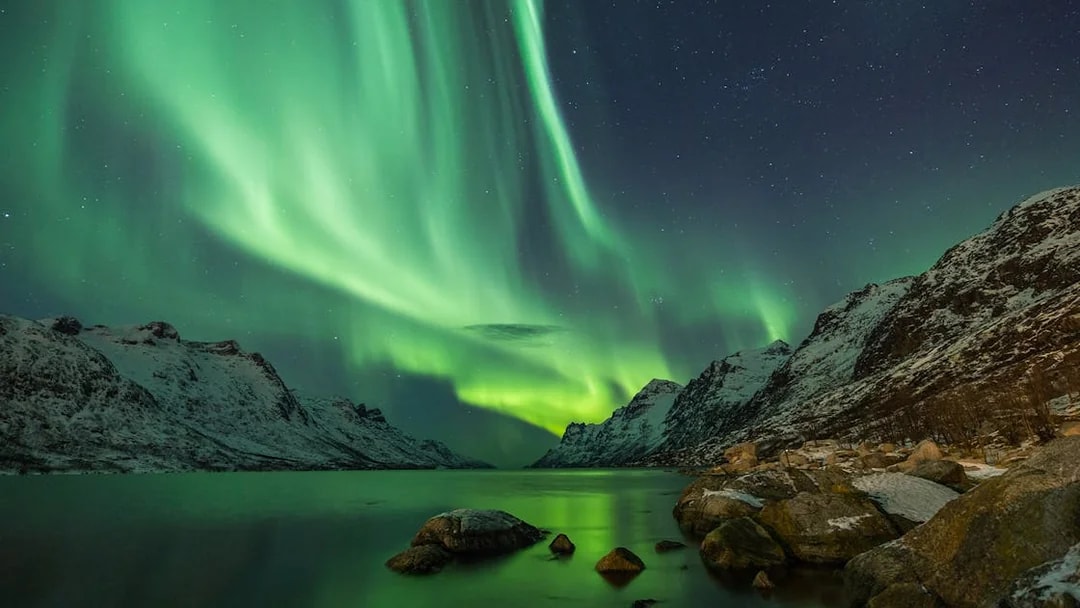 Northern lights over snowy mountains and a lake in Tromso.