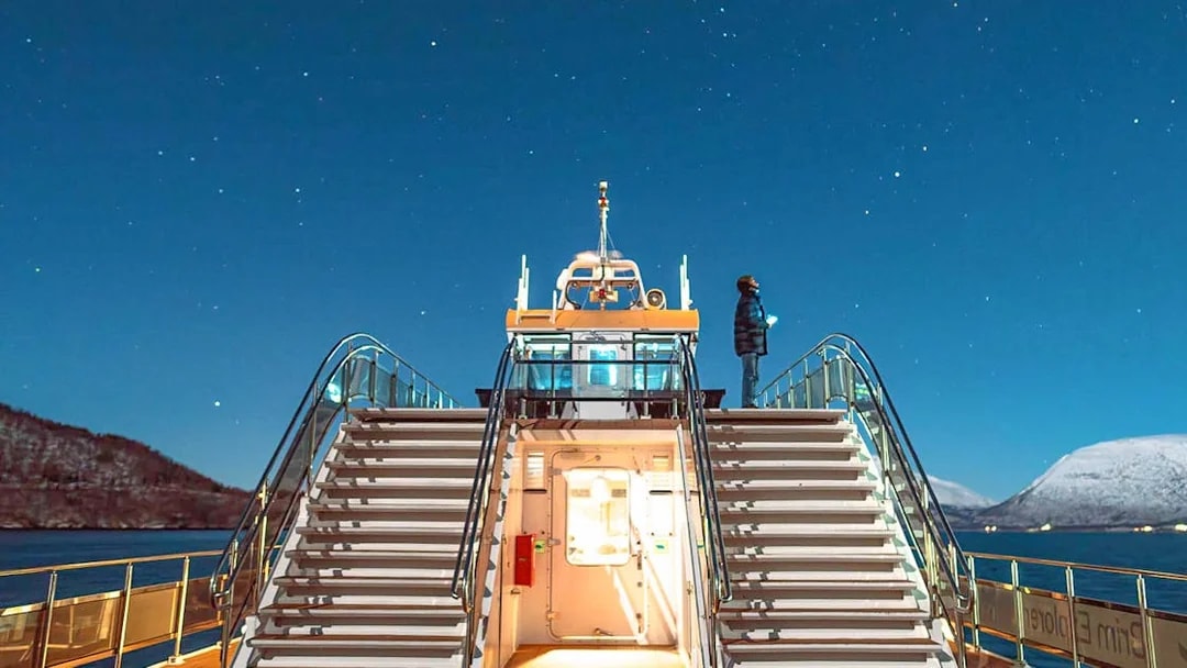 Cruise ship deck under starry sky in Tromso, Norway, with person observing the Northern Lights.