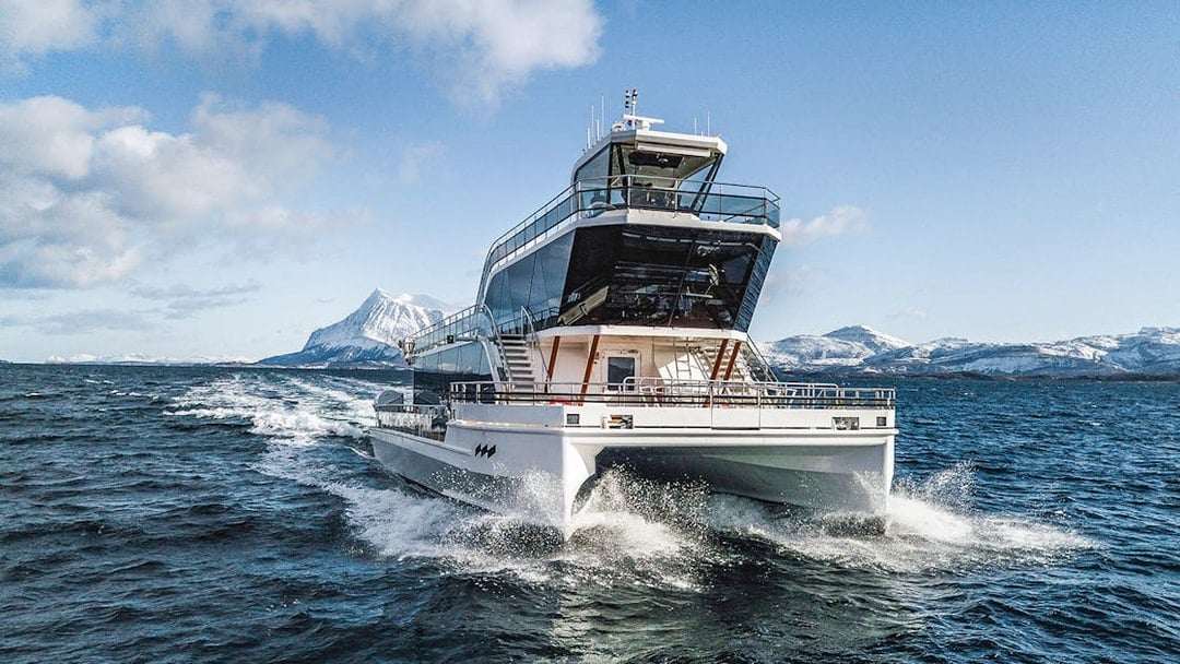 Silent whale watching boat in Tromso fjord with snowy mountains in the background.