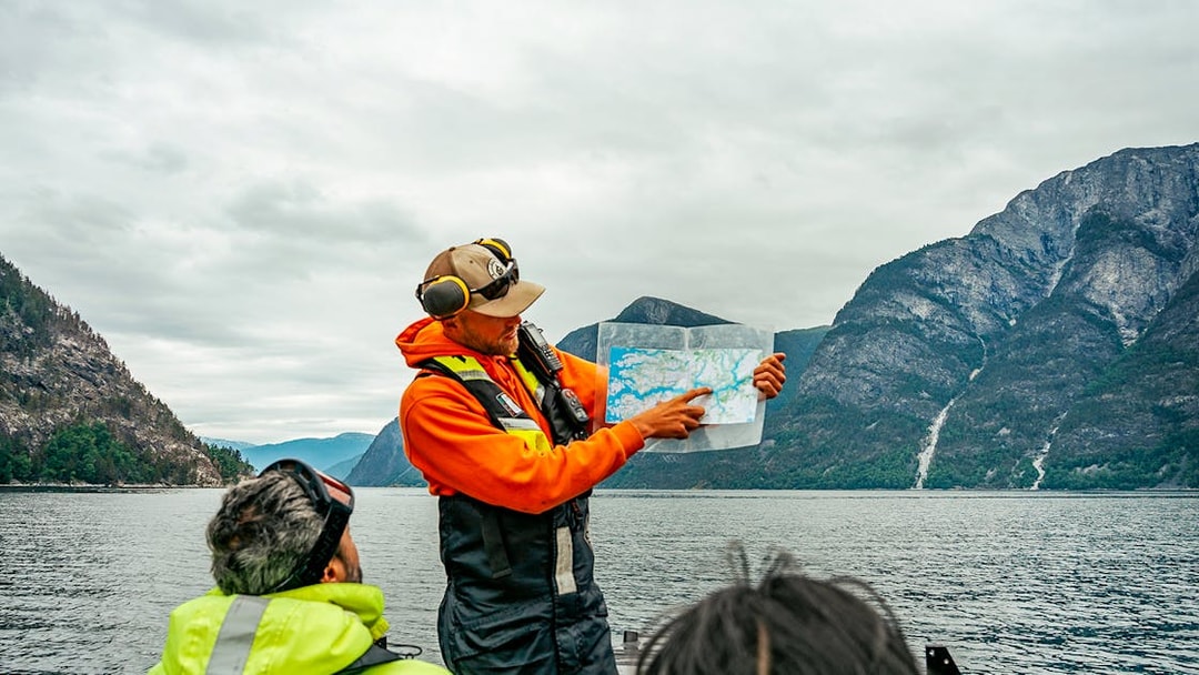 Guide showing map on RIB boat during Tromso whale safari with mountains in background.