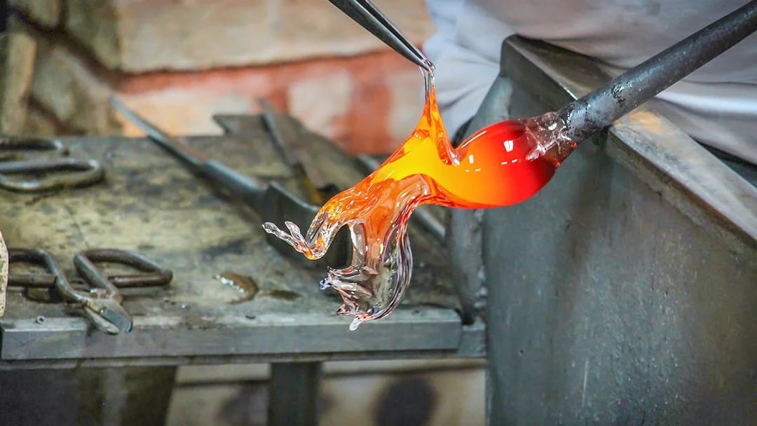 Glass artist shaping molten glass in Murano workshop.