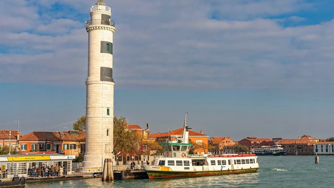 Ferry arriving at Murano, Italy, with colorful buildings and a lighthouse by the canal.