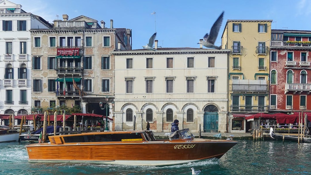 Speedboat cruising Venice canal with historic buildings in the background.