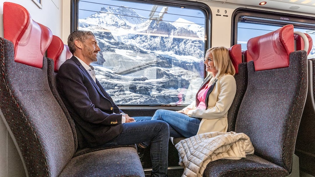 Passengers enjoying scenic views on Jungfraujoch Railway with snowy mountains in background.