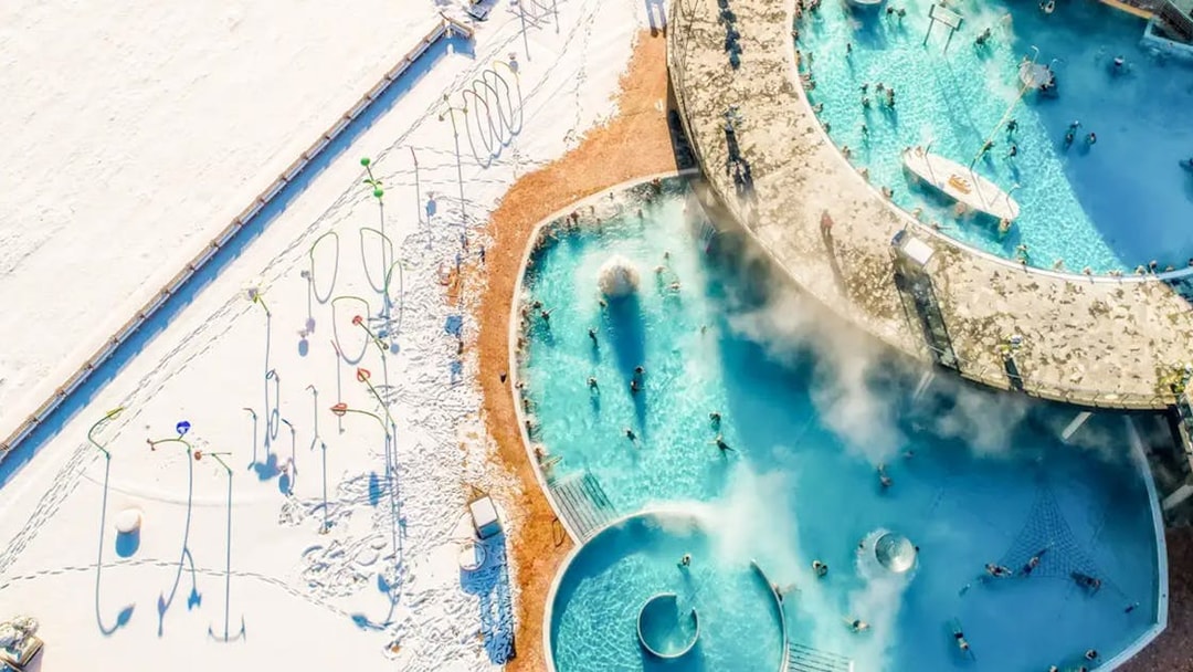 Aerial view of Chocholow Thermal Baths with people enjoying the warm pools surrounded by snow.