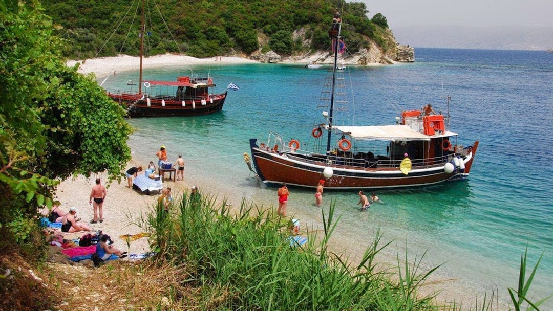 Boat anchored near a beach in Corfu with people enjoying a BBQ and swimming.