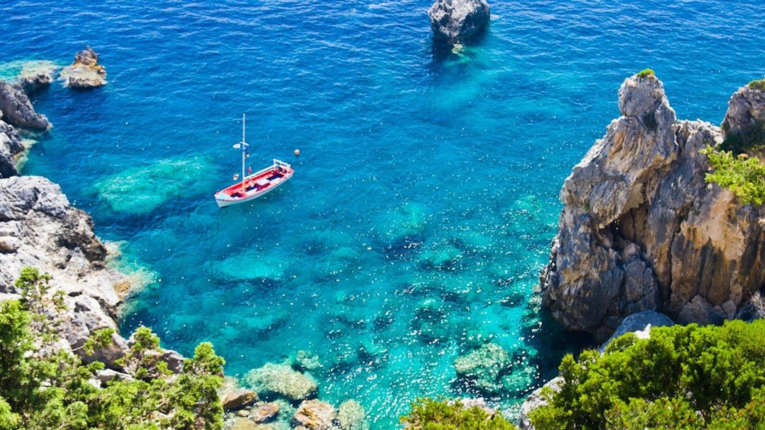 Boat sailing in clear blue waters near rocky coastline in Corfu.