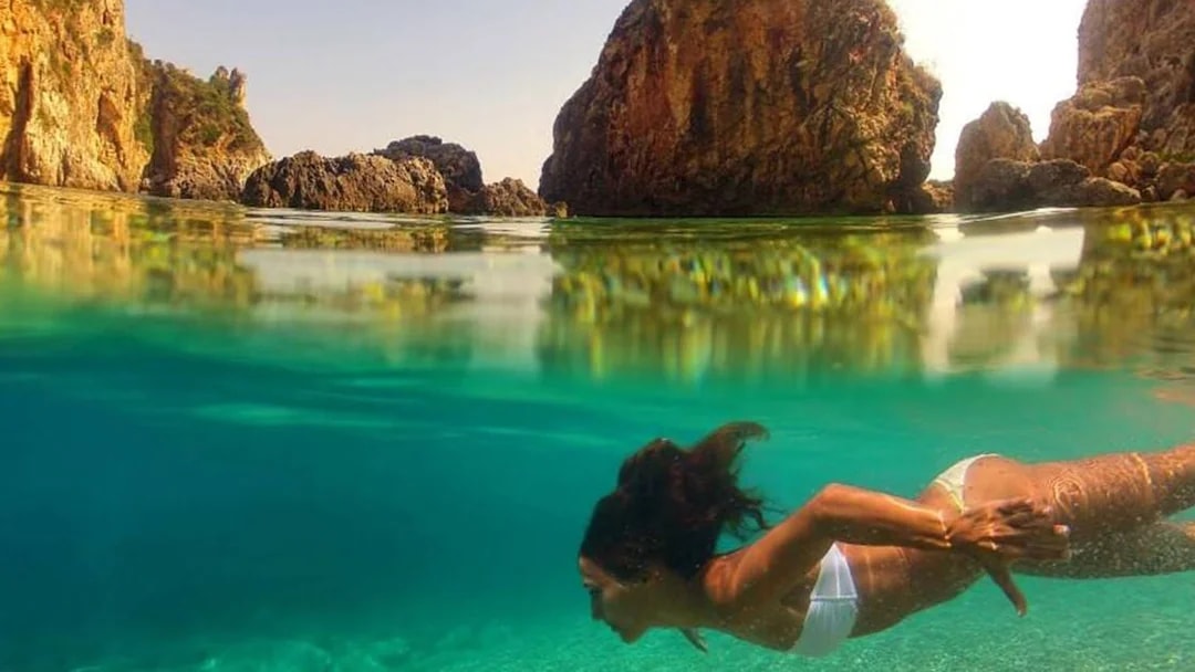 Snorkeler exploring clear waters near rocky cliffs in Corfu during a full-day boat trip with BBQ.
