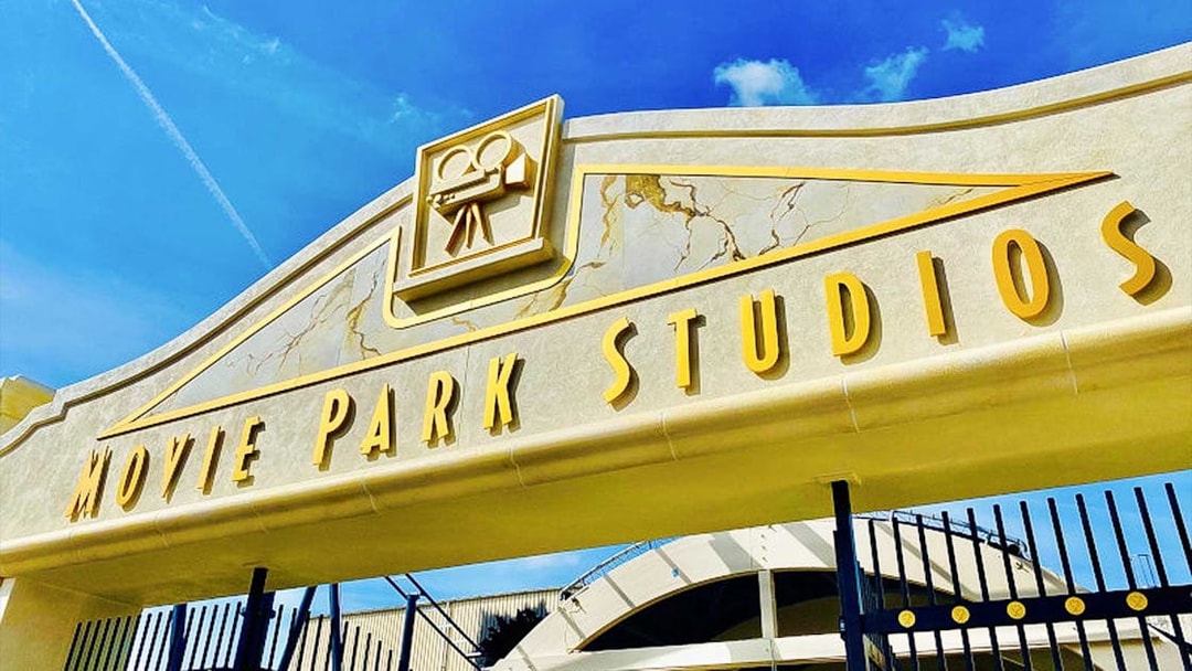 Movie Park Studios entrance gate with film camera icon under blue sky.